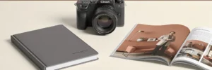 Camera op wit bureau naast een leren jaarverslag en een open tijdschrift, in een minimalistische compositie met ivoor- en terracottatinten.