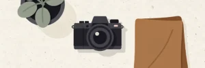 Minimalistische camera, ingepotte plant en warm stoffen staal op wit studiodek in stijlvolle flat-lay compositie.