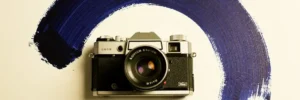 Vintage camera naast een expressief kobaltblauwe penseelstreek op ivoor achtergrond, minimalistisch bovenaanzicht.